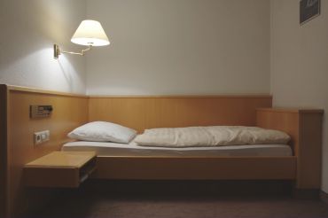 A simple, single bed with white bedding in a modest room.