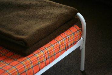 Folded brown blanket on a plaid-patterned bed with white metal frame.