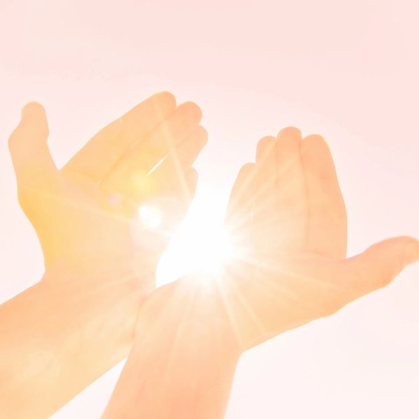 Hands catching bright sunlight against a soft pink sky.