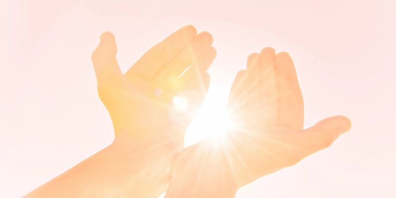 Hands forming a shape around the bright sun with a soft pink background.