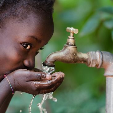 A young girl cups her hands to drink water under a running tap.