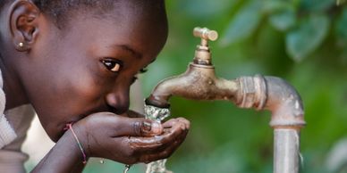 picture of a young person using their hands to catch water from a faucet and drink the water.