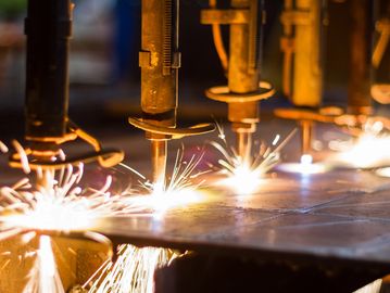 Industrial machines cutting metal with bright sparks flying.