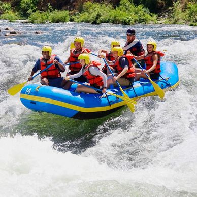 Group of people white water rafting on a river with safety gear.