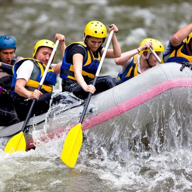 Group of people white-water rafting with yellow helmets and paddles.