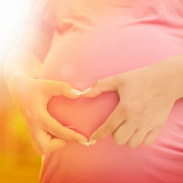 Woman folding her hands in the shape of a heart over her belly bump.