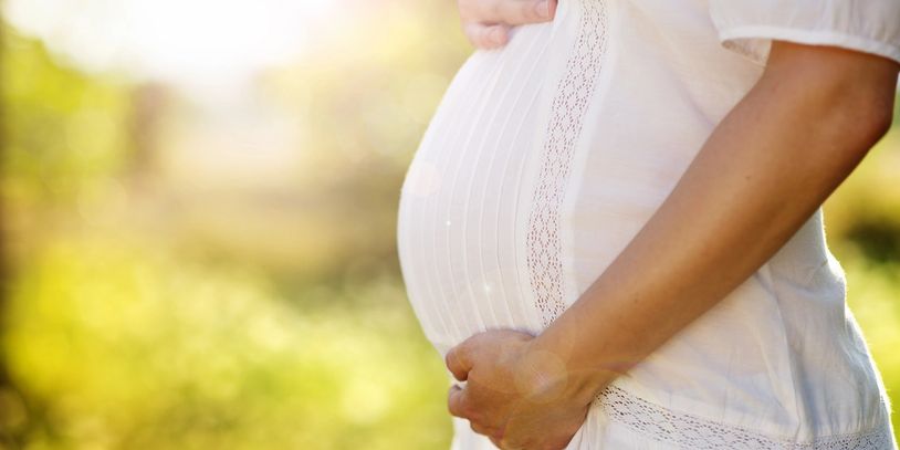Pregnant woman holding her belly in sunlight.