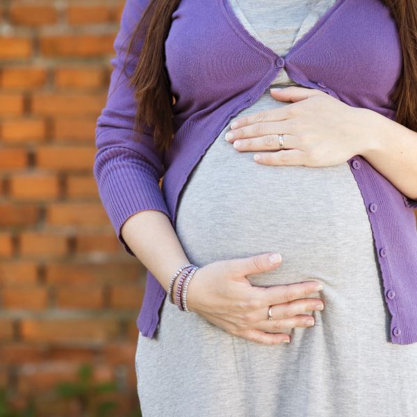 Pregnant woman gently holding her belly wearing a purple cardigan.