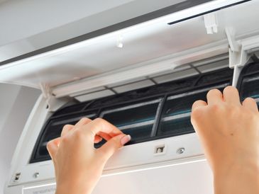 Hands cleaning filters inside a wall-mounted air conditioner