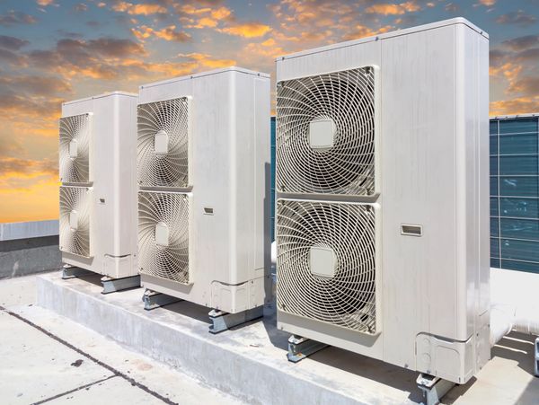 Three large air conditioning units on a rooftop at sunset.