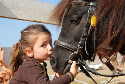 A young girl affectionately kissing a black horse's muzzle.
