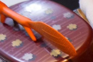 Orange fly swatter on a patterned surface.
