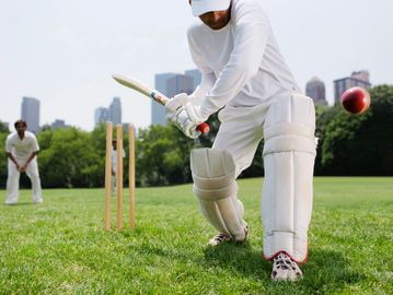 A cricket batsman in white gear playing a shot on a grassy field.
