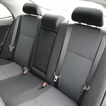 Clean, gray fabric backseat of a car with seat belts and headrests.