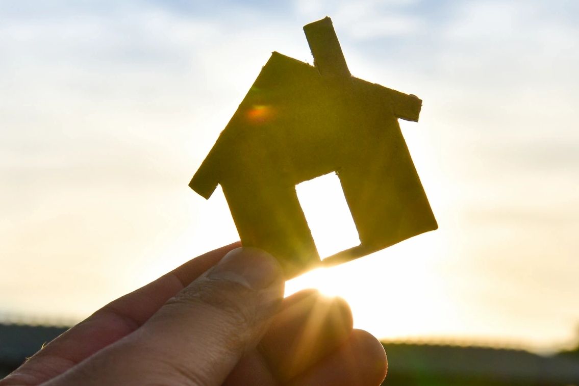 Hand holding a small house cutout against the sun.