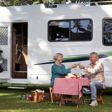 Couple toasting with drinks outside their camper on a sunny day.