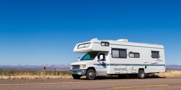 White RV parked on a desert highway under a clear blue sky.