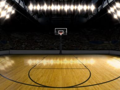 Empty basketball court with bright overhead lights in a dark arena.