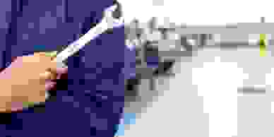 An automotive workshop in the background with a mechanic's torso and hand holding a spanner.