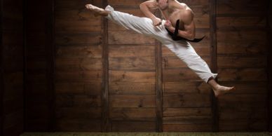 Martial artist performing a flying kick indoors.