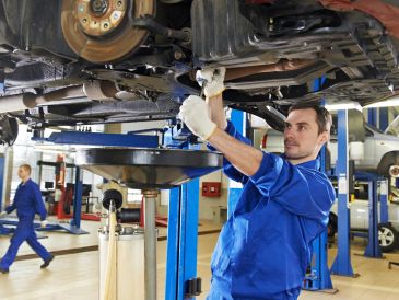 Mechanic repairing car undercarriage in a service garage.