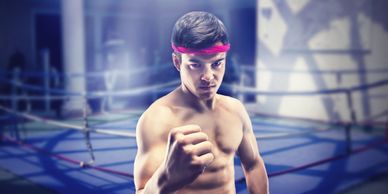A young male boxer with a red headband poses confidently in a boxing ring.