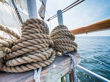 Thick ropes coiled around posts on a sailing boat by the sea.
