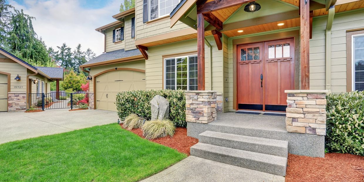 Modern suburban house entrance with wooden double doors and manicured lawn.
