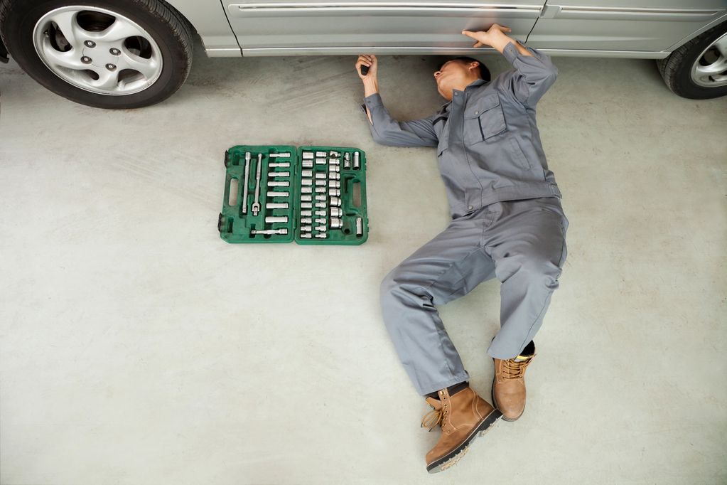 Mechanic inspecting under a car with tools nearby.