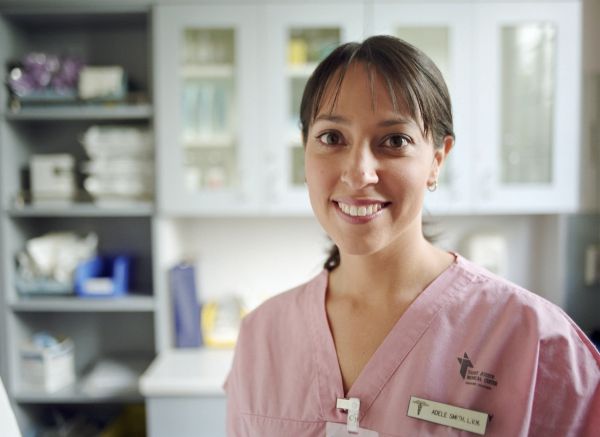 Smiling nurse in pink scrubs in a medical setting.