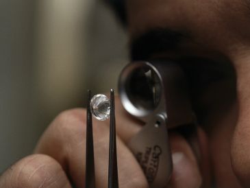 Person inspecting a diamond with tweezers and magnifier.