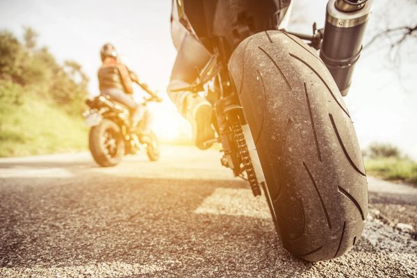 Close-up of motorcycle tire with rider and another motorcycle in the background.