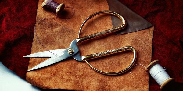 An image of a thread roll and a scissor placed on top of a leather piece. 