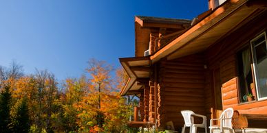 Cozy wooden cabin with white chairs against a vibrant autumn backdrop.