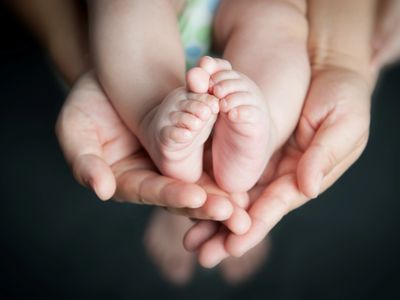 Adult hands gently holding a baby's tiny feet.