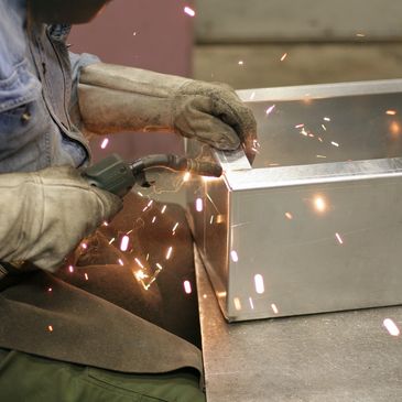 Person welding a metal box with sparks flying.