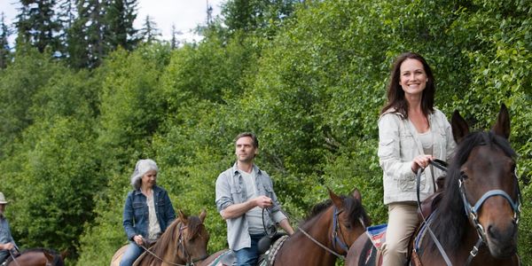 Four people horseback riding in a forested area.