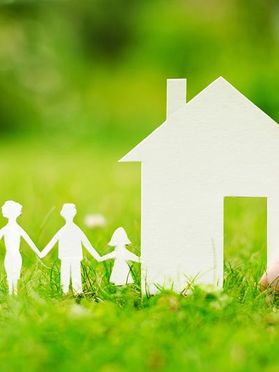 Paper cutout family holding hands next to a house on grass.