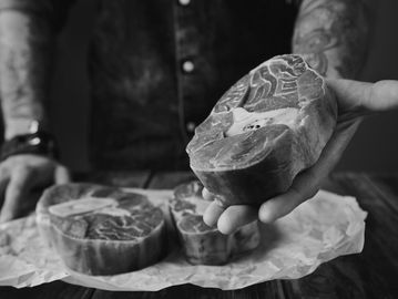Person holding a raw beef steak with more steaks on parchment paper.