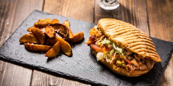 Grilled sandwich with crispy potato wedges on a slate serving board.