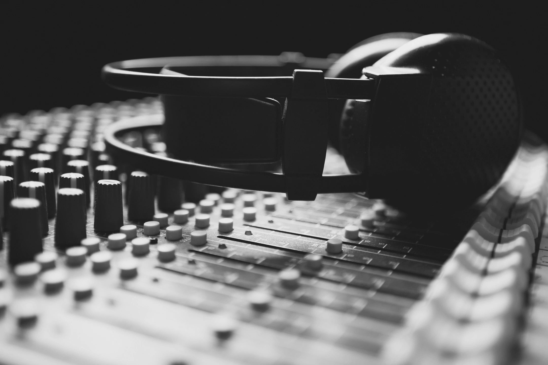 Black headphones resting on an audio mixing console with various knobs and sliders.
