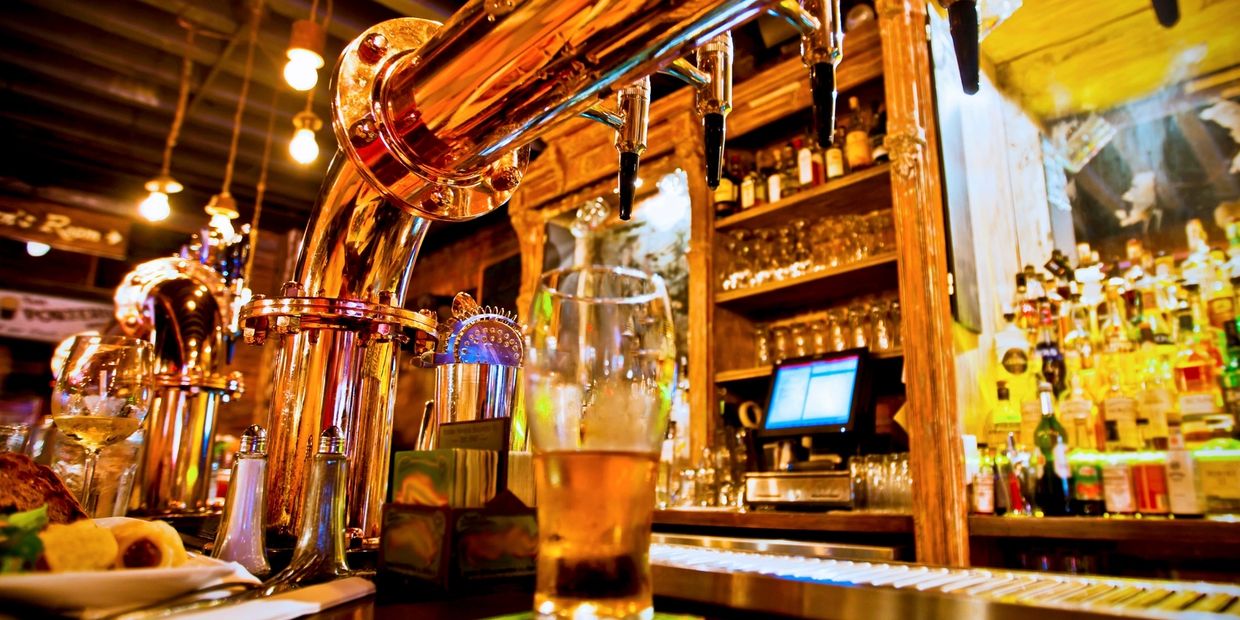 Close-up of a half-filled pint under beer taps at a brightly lit bar