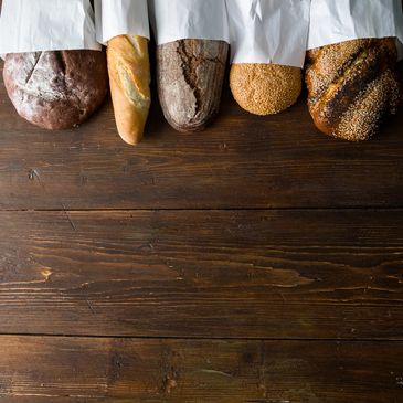 Five different types of bread wrapped in white paper on a wooden surface.