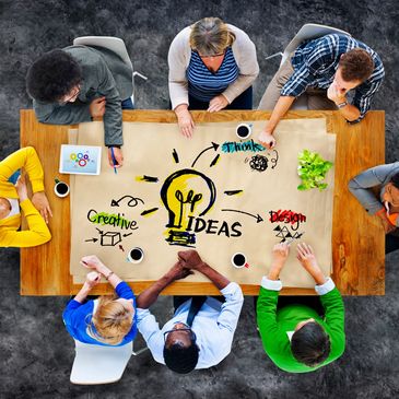 View down on a table of 8 people discussing & drawing on a Piece of brown paper-Idea image shown  