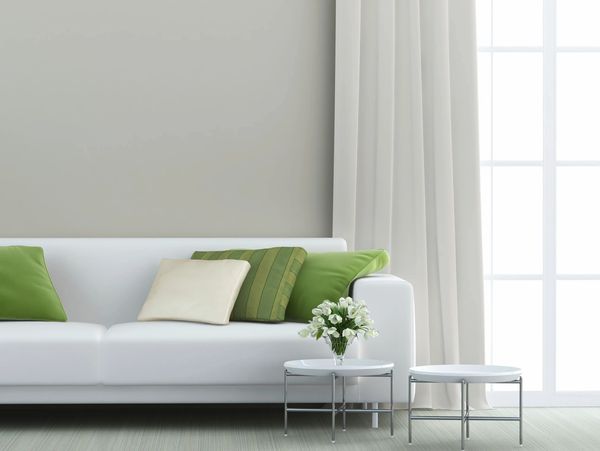Modern white sofa with green cushions and small round tables with flowers in a bright living room.