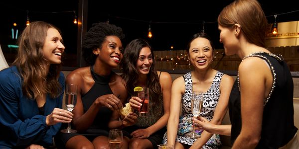 Five women enjoying drinks and conversation at a lively evening gathering.