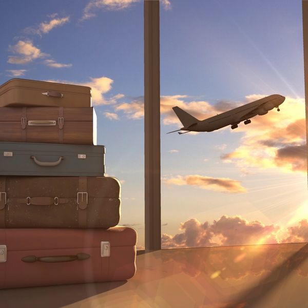 Stacked suitcases near airport window with plane taking off at sunset.