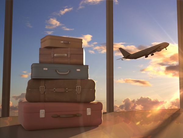 Stacked vintage suitcases near a window with a plane taking off at sunset.