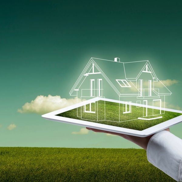 Hand holding a tablet displaying a virtual house model on a grassy field.