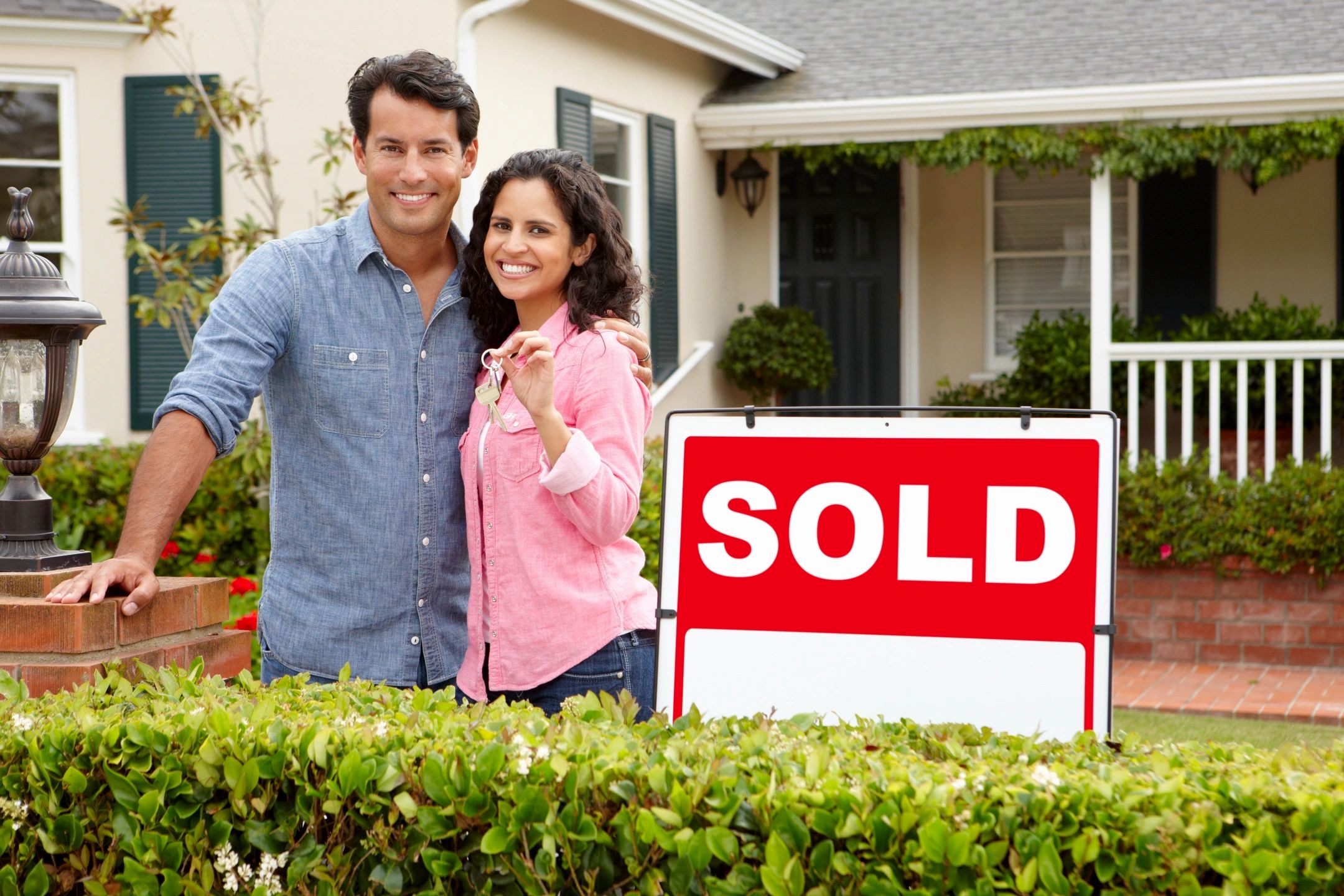 Couple holding the key to new home in front of Sold sign. 